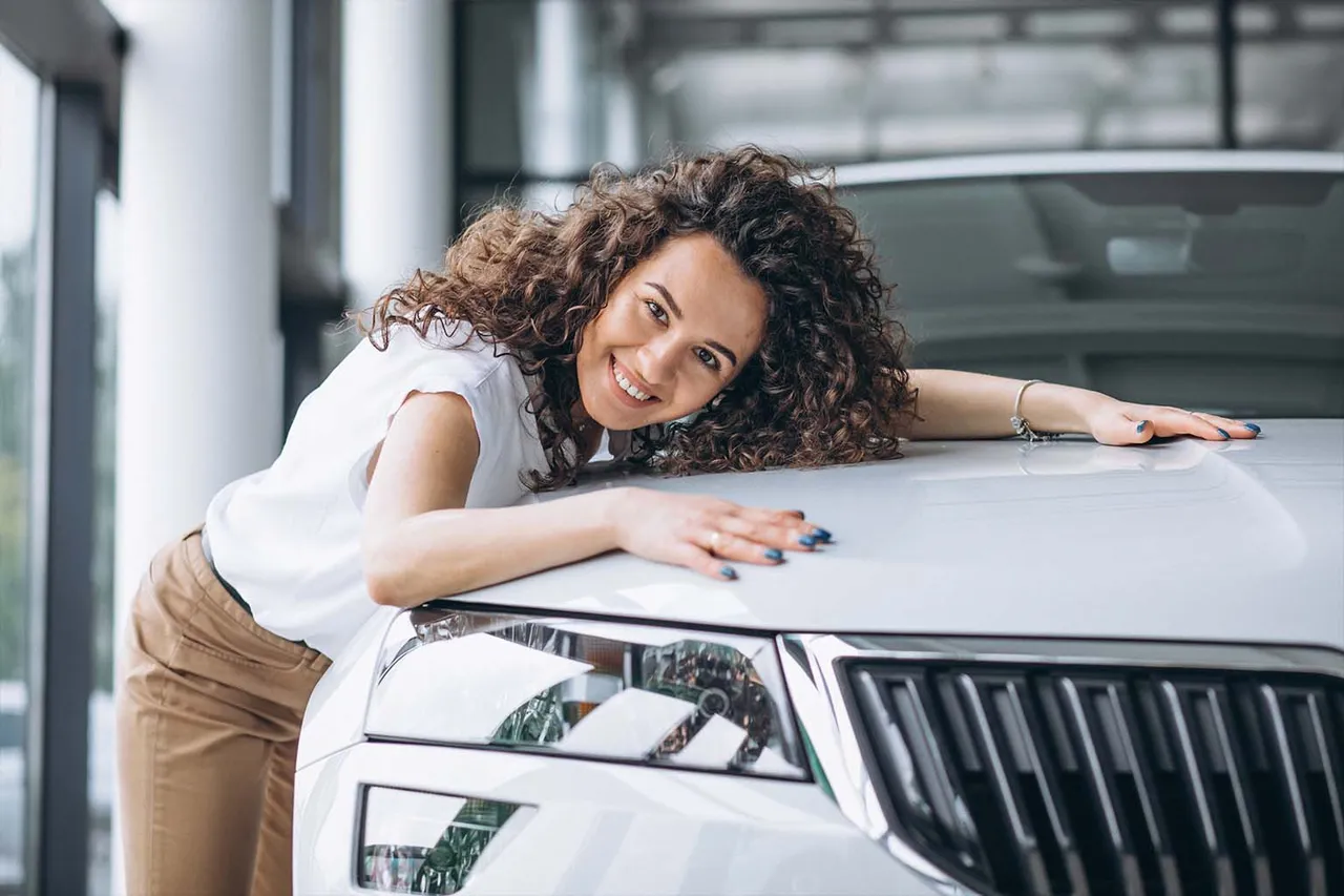 Mulher sorridente abraça o capô de um SUV prata em uma concessionária, celebrando a ampliação do poder de compra com o Crédito em Dobro Consórcio Mapfre.