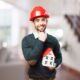 Homem com capacete de obra e uma casinha nas mãos, simbolizando o consórcio para construção de imóveis.