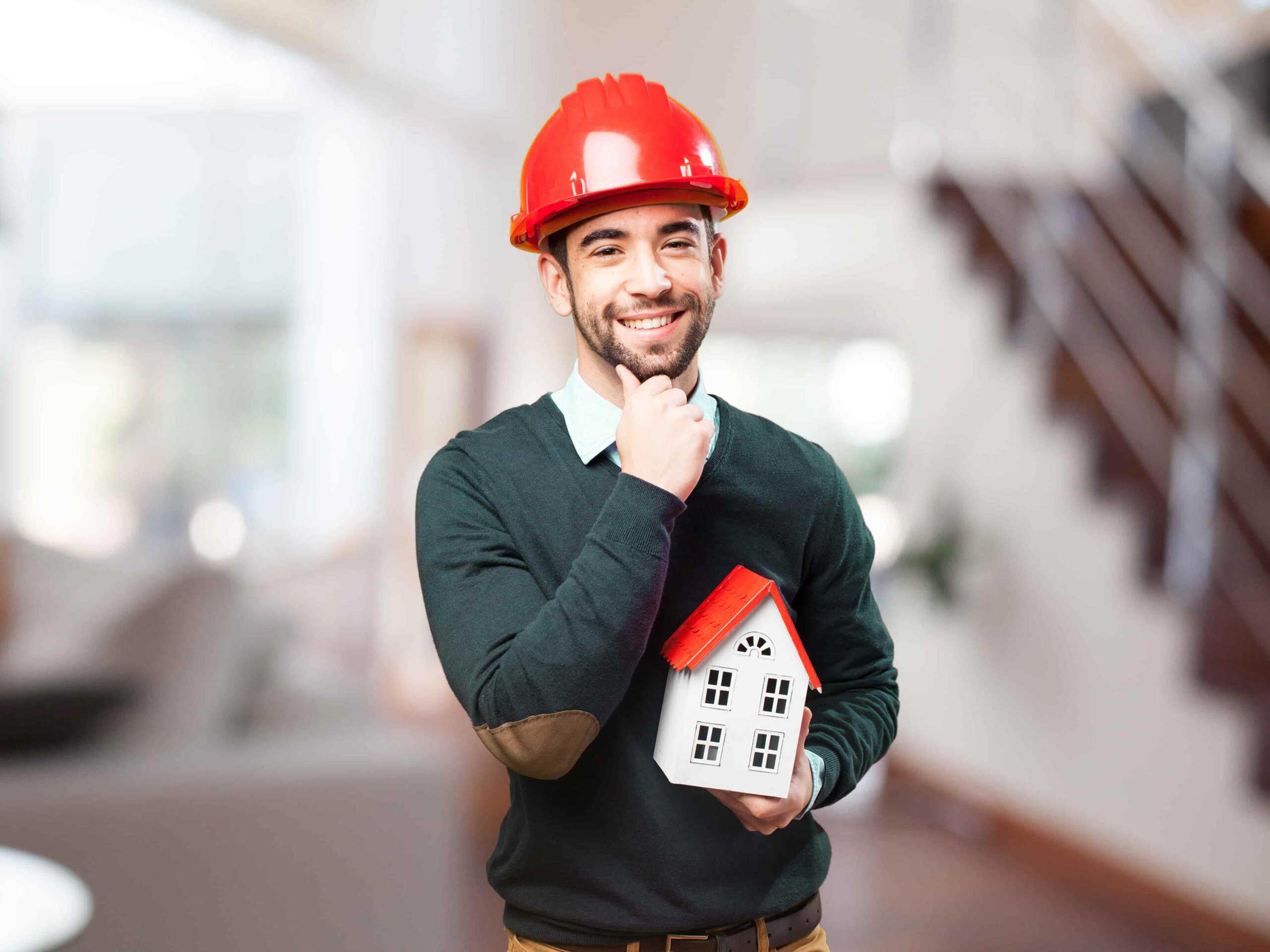 Homem com capacete de obra e uma casinha nas mãos, simbolizando o consórcio para construção de imóveis.